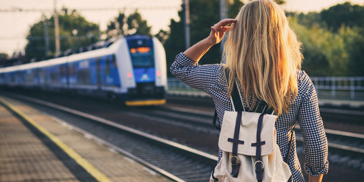 En kvinna med ryggsäck står på en perrong där ett tåg är på väg in.