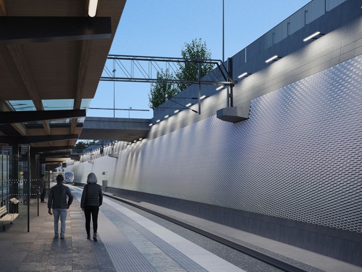 På plattformen går två personer i riktning mot betongtunneln och till vänster syns konstverket i kvällsljus.