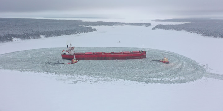 Stort rätt fartyg på en yta där isen i älven brutits upp, i ett snöigt landskap