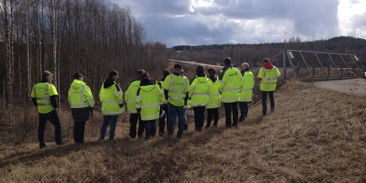 Människor i varselkläder i grupp ute i fält.