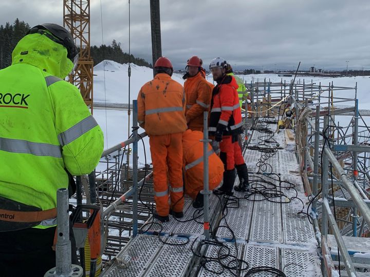 Varselklädda medarbetare står på byggarbetsplats, molning himmel i vinterlandskap