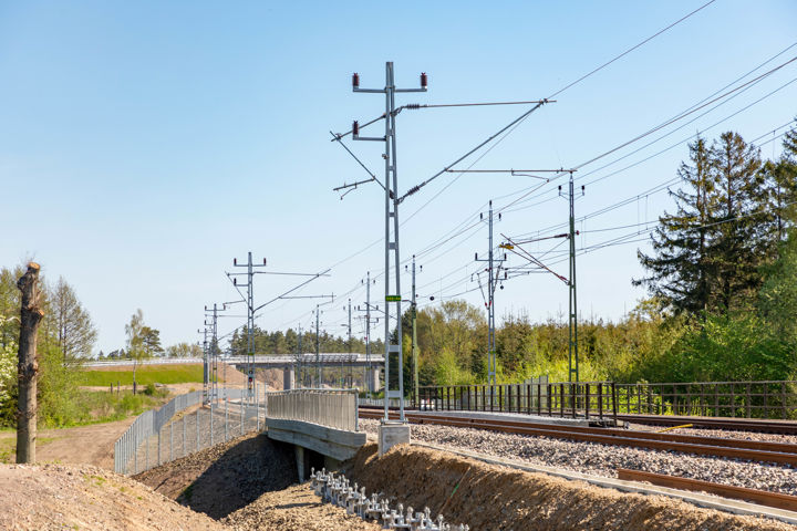 Bild med järnvägsbro med två järnvägsspår. Kontaktledningar syns i luften mot en ljusblå himmel.
