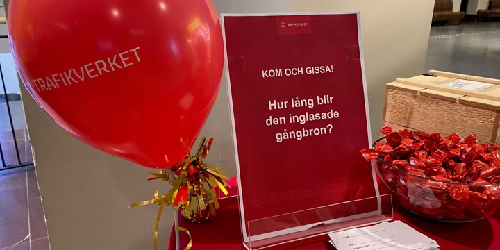 En röd ballong som det står Trafikverket på. En skylt med text om tävling, svarslappar och godis med rött papper på ett bord med röd duk.