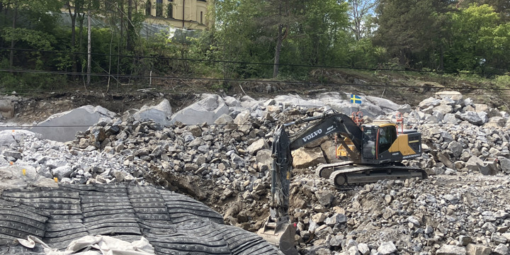 Pågående sprängarbeten nedanför Skönsmons kyrka. En grävmaskin står bland sprängsten och sprängmattor ligger utlagda.