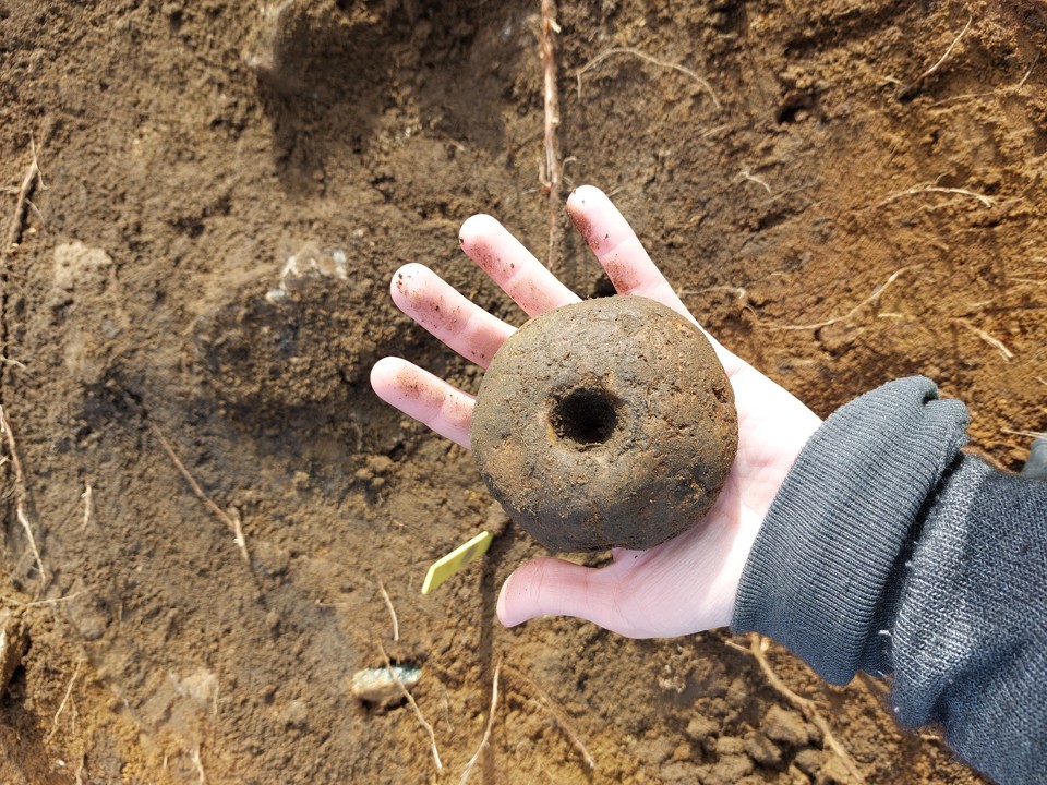 En hand håller i ett arkeologiskt fynd som är runt av järn