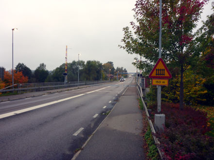 Väg 250, väg med två körfält, en skylt som varnar för järnvägsövergång, några träd till höger om vägen.