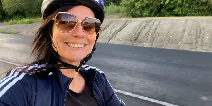 En glad kvinna i cykelhjälm och solglasögon med solens strålar cyklar med ett stort leende.