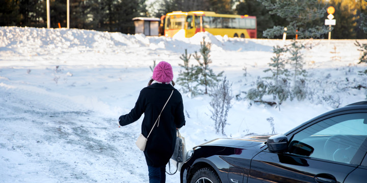 En kvinna har parkerat sin bil och går till en väntande buss vid en busskur. Det ligger snö på marken.