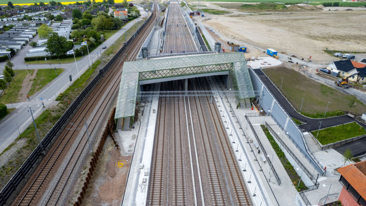 En flygbild över en tågstation med fyra spår.  Vänster om stationen går ytterligare två järnvägsspår. Över stationen sträcker sig en bro som är täkt med grönt glas.