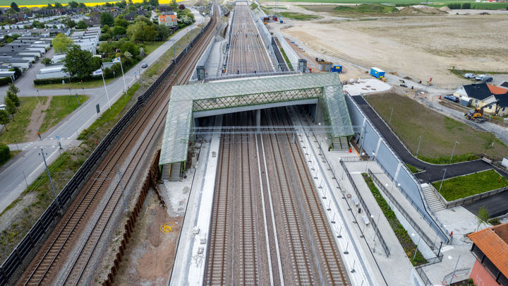 En flygbild över en tågstation med fyra spår. Vänster om stationen går ytterligare två järnvägsspår. Över stationen sträcker sig en bro som är täkt med grönt glas.