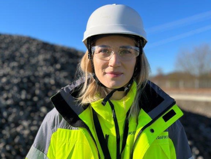 Bild på en av projeketets medarbetare Elin Larsson i gula kläder och vit hjälm med en blå himmel som bakgrund.