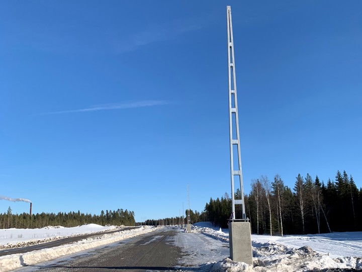 väg med höga metallstolpar på höger sida, mot en blå himmel