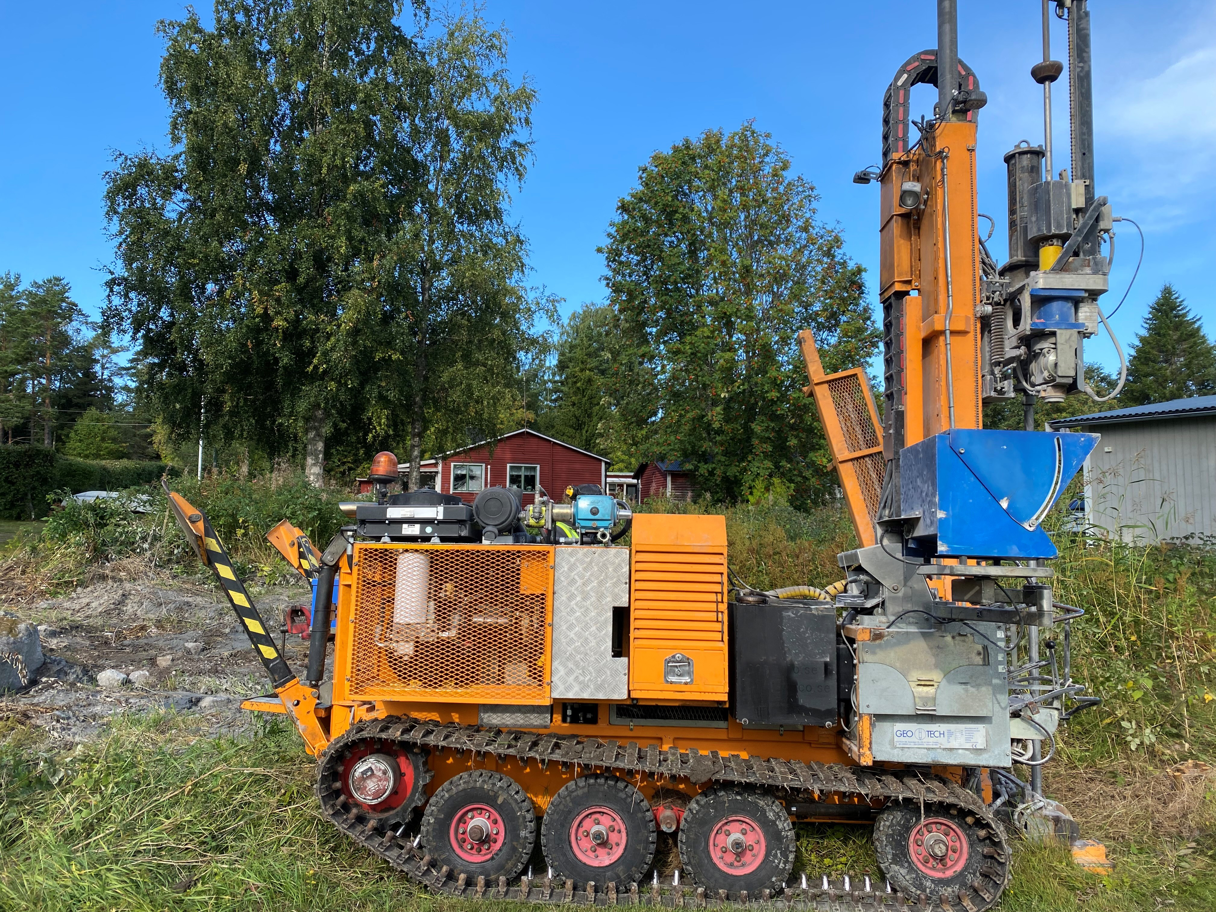 Bild på en borrbandvagn vid ett grönområde intill två fastigheter.