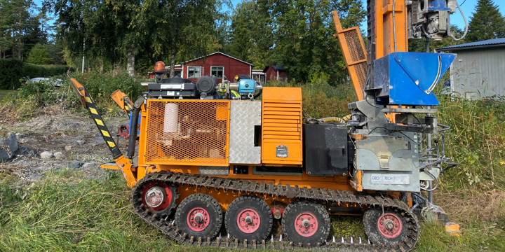 Bild på en borrbandvagn vid ett grönområde intill två fastigheter.