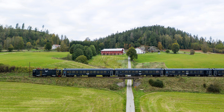 Tåg åker över bro över mindre väg i odlingslandskap.