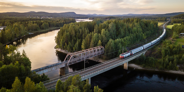 Vy över en älv med två broar varav ett tog är på väg över den ena. Solnedgång.