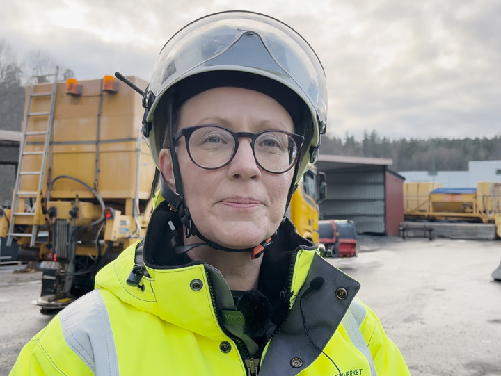 Människa i gula varselkläder framför plogfordon.