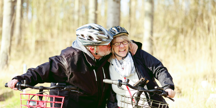 Äldre man och kvinna går med cyklar, cykelhjämar på huvudet
