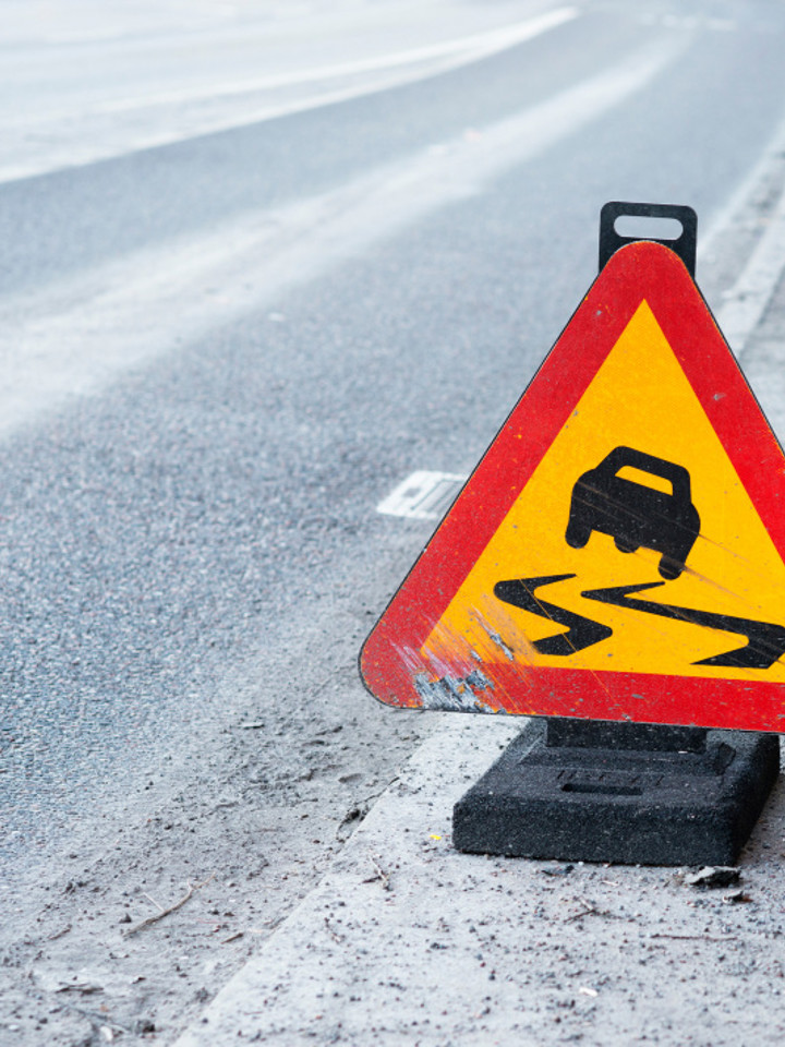 Triangelformat vägskylt placerad längs väg med snö. På skyltens syns en illustrerad bil med halkspår.