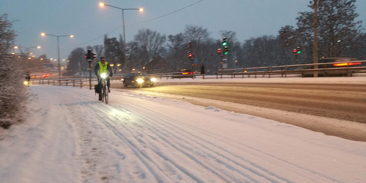 Cyklist i stadstrafik på snöig cykelbana, lampan lyser, det är skymning.