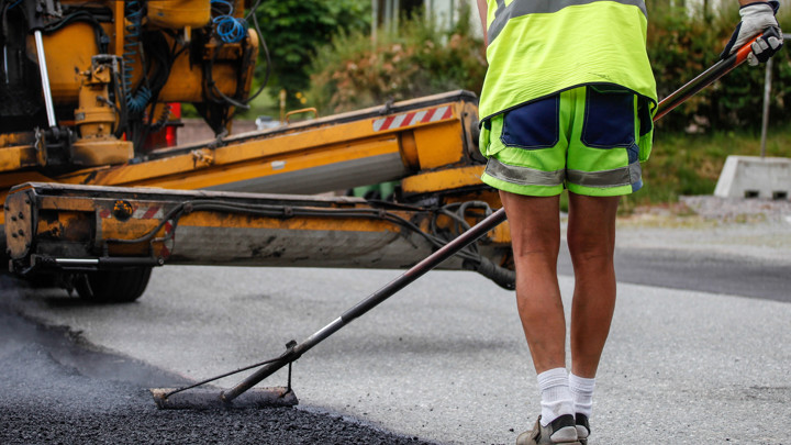 I bilden syns en person med gula kläder som arbetar med beläggning på vägen.