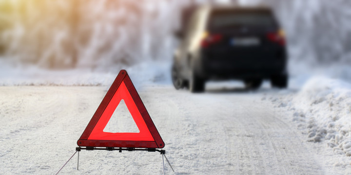 Väg med snö- I bildens syns en varningstriangel och en bil som står längs vägen.