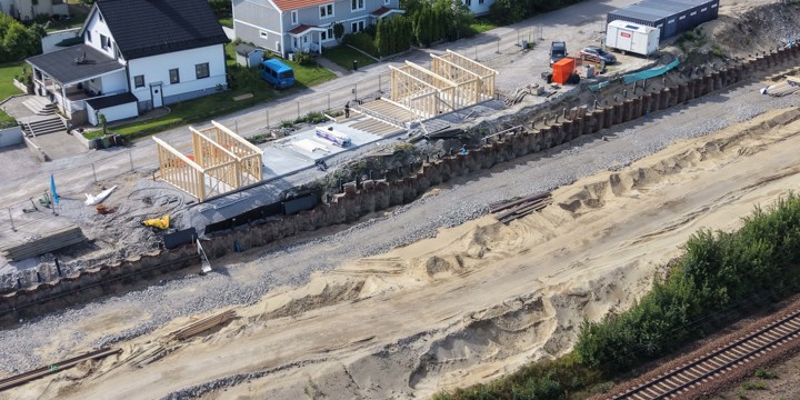 Befintlig järnväg sträcker sig i en kurva in mot centrala Sundsvall. På ena sidan järnvägen är Sönderborgsgatan en tillfällig grusväg och i arbetsområdet är ett flertal maskiner. Utkikstornet skymtar på Norra berget i bakgrunden samt några flerfamiljshus.