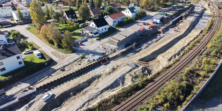 Befintlig järnväg sträcker sig i en kurva in mot centrala Sundsvall. På järnvägens västra sida pågår markarbeten för ett till spår, arbeten med en stödkonstruktion av stål och byggnation av en ny carport intill ett bostadsområde.