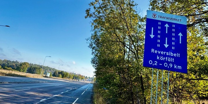 Blå skylt bredvid en väg. Skylten informerar med text och pilar om reversibelt körfält.