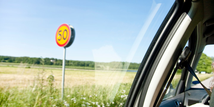 50-skylt vid fält syns genom bilfönster i förbipasserande bil.