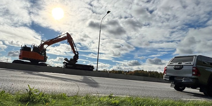 Väg i motljus, med grävmaskin i bakgrunden. 