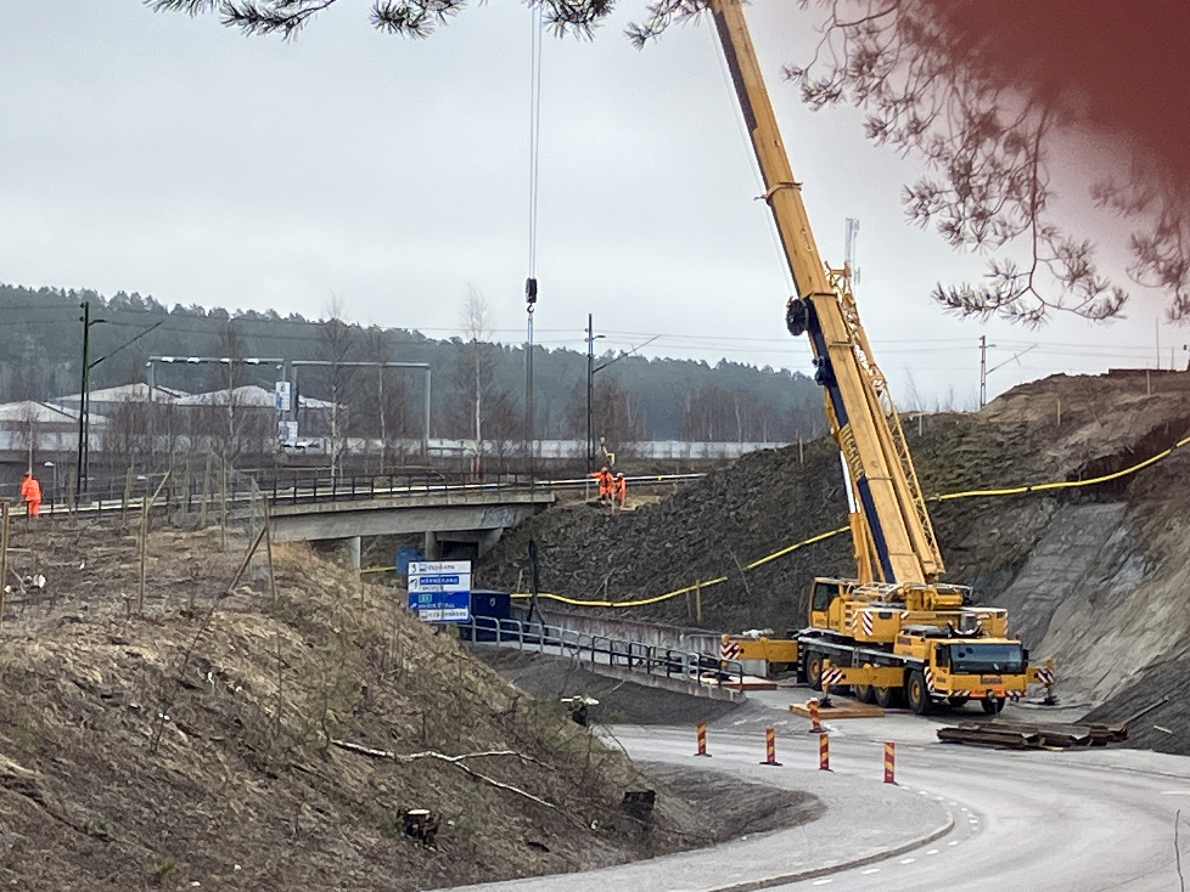 Spontarbeten vid Björneborgsgatan. Vid järnvägsbron står stor och en hög byggkran som upptar gång- och cykelvägen. Kranen lyfter upp stålspont upp mot järnvägen där varselklädda arbetare står. 