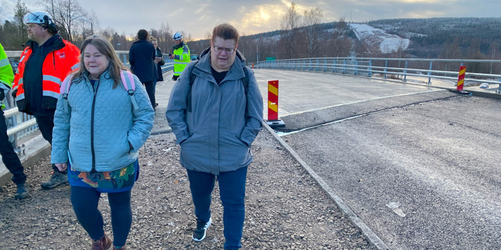 Två kvinnor passerar över bron förbi några byggarbetare.