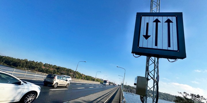 Svartvit skylt bredvid en väg på en bro. Skylten har pilar som pekar uppåt och nedåt.