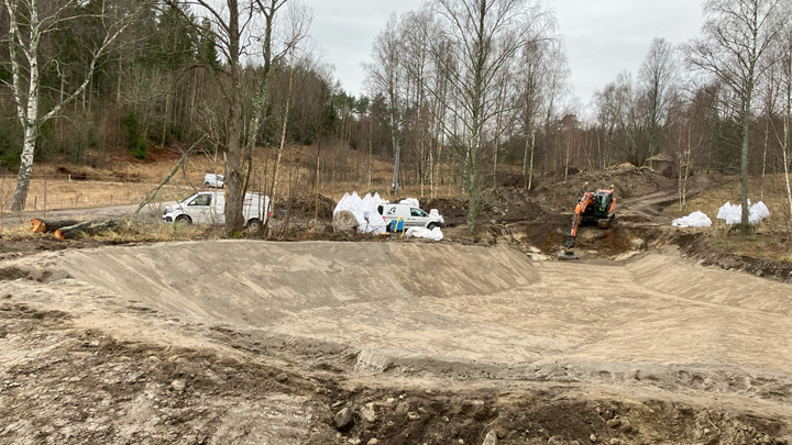 Damm under uppbyggnad, bilar och grävmaskin i bakgrunden.