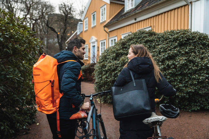 Två vuxna, en man och kvinna, drar sina cyklar på väg mot en fastighet.