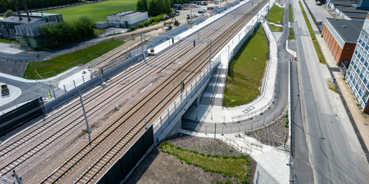 En flygbild på station med fyra spår och plattformar vid ytterspåren. På höger sida om stationen går en gata med kontorshus. På vänster sida om stationen är det en park.